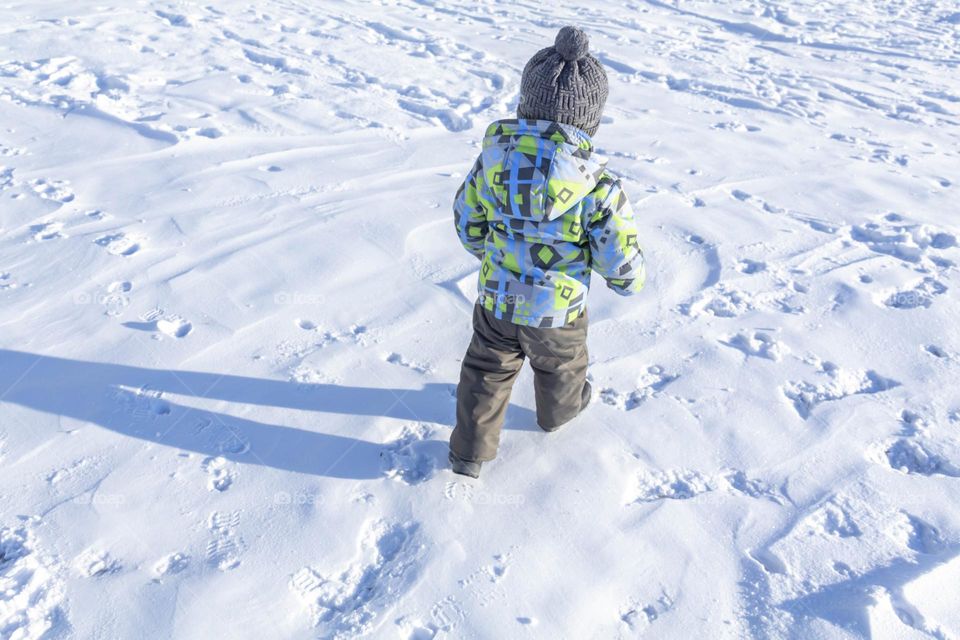 A child with a serious expression on his face in winter clothes jackets, pants, hat and boots in winter on the white snow on the street and in the park in nature plays winter fun.