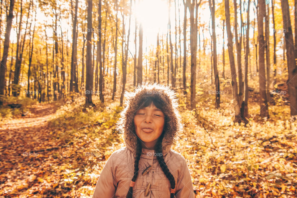 Cute little girl is making faces in a sunny autumn forest