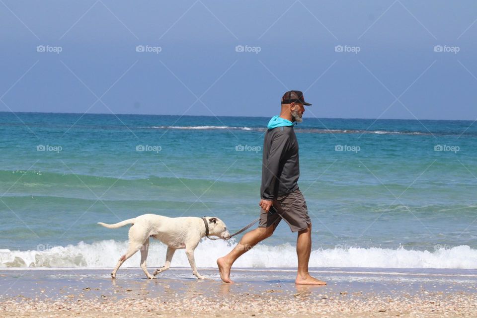 A man walking with his dog on the beach