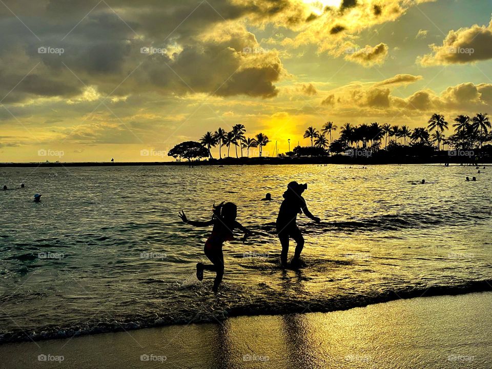 Silhouetted figures playing in the surf at sunset 
