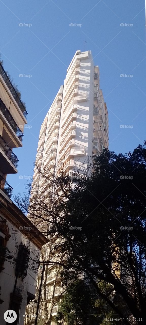 edificio blanco con balcones y su sombra en entre casa pequeñas y edificio bajos y arboleras