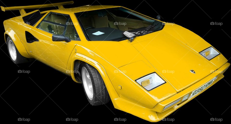 ISOLATED on BLACK,
Yellow Lamborghini Countach
is a mid-engined, V12 sports car produced by Italian car manufacturer Lamborghini from 1974 to 1990. Its design pioneered and popularized the wedge-shaped, sharply angled look popular in many high-performance sports cars. It also popularized the "cab forward" design concept, which pushes the passenger compartment forward to accommodate a larger engine.
In 2004, American car magazine Sports Car International named the car number three on the list of Top Sports Cars of the 1970s, and listed it number ten on their list of Top Sports Cars of the 1980s.
The rear wheels were driven by a traditional Lamborghini V12 engine mounted longitudinally with a mid-engined configuration. This contrasted with the Miura with its centrally mounted, transversely-installed engine. For better weight distribution, the engine is pointed "backwards"; the output shaft is at the front, and the gearbox is in front of the engine, the driveshaft running back through the engine's sump to a differential at the rear. Although originally planned as a 5 L (310 cu in) powerplant, the first production cars used the Lamborghini Miura's 4-liter engine. Later advances increased the displacement to 4754 cc and then (in the "Quattrovalvole" model) 5167 cc with four valves per cylinder.
All Lamborghini Countaches were equipped with six Weber carburetors until the arrival of the 5000QV model, at which time the car became available in America, and used Bosch K-Jetronic fuel injection. The European models, however, continued to use the carburetors (producing more power than fuel-injected cars) until the arrival of the Lamborghini Diablo, which replaced the Countach.