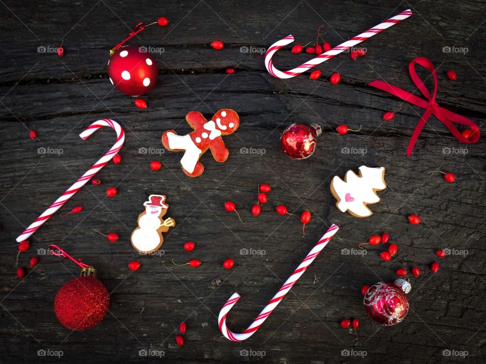 Flat lay of red and white Christmas decorations consisting of candy canes,gingerbread,red ribbon, red globes and red berries on rustic wooden table