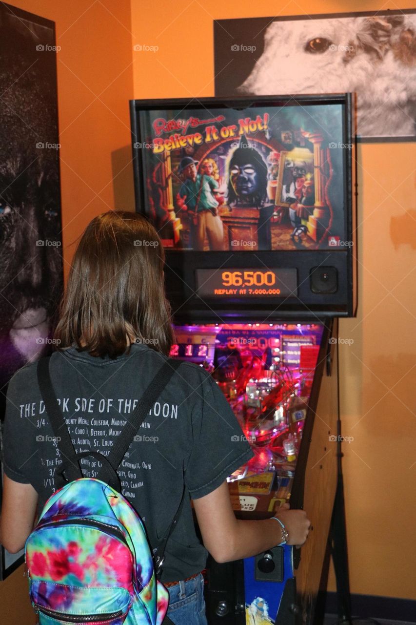 Women playing an extremely fun pinball machine, enjoying the entertainment while wearing her trusty backpack as she navigates the world 
