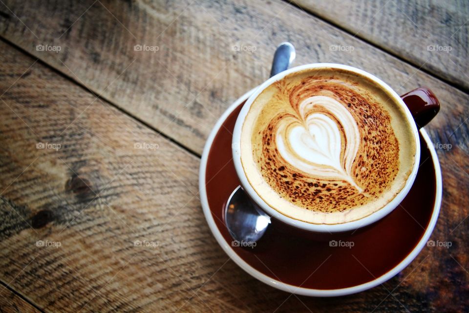 A cup of coffee on a wooden table with a heart shaped pattern on it's surface.