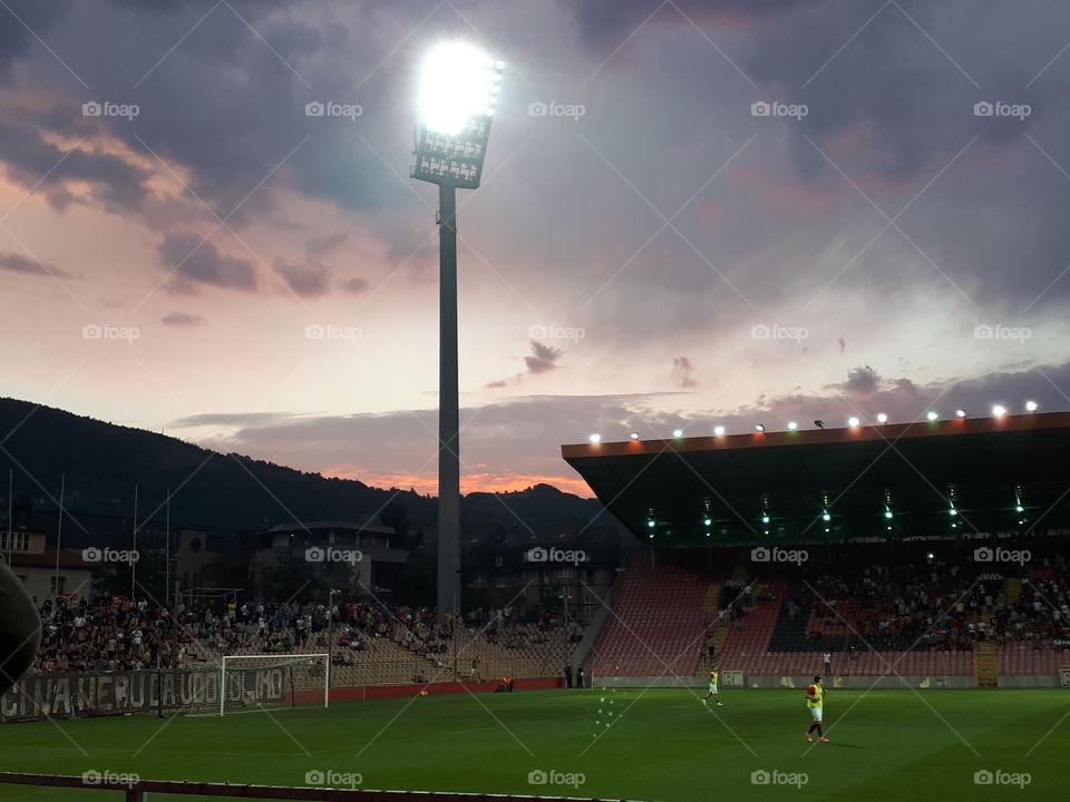 sunset behind the Bilino Polje stadium while the game is running, and the reflectors slowly fall