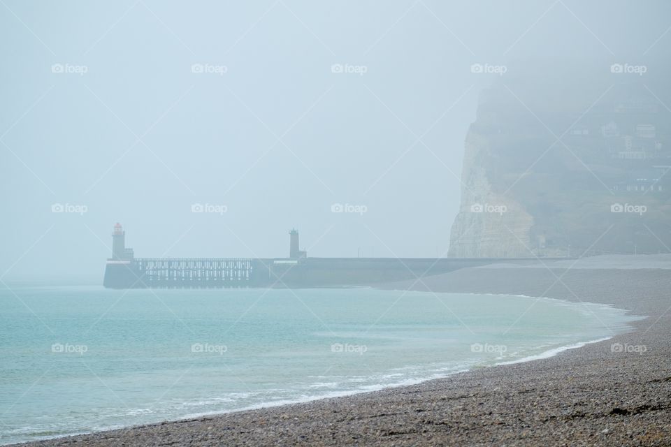 Fécamp, Normandy Beach with the white chalk rocks on a grey misty day showing the lighthouses of the port in the distance 