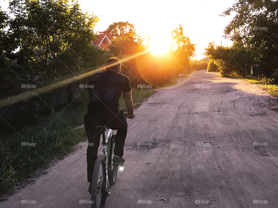 Young man riding a bicycle by the road at sunset 