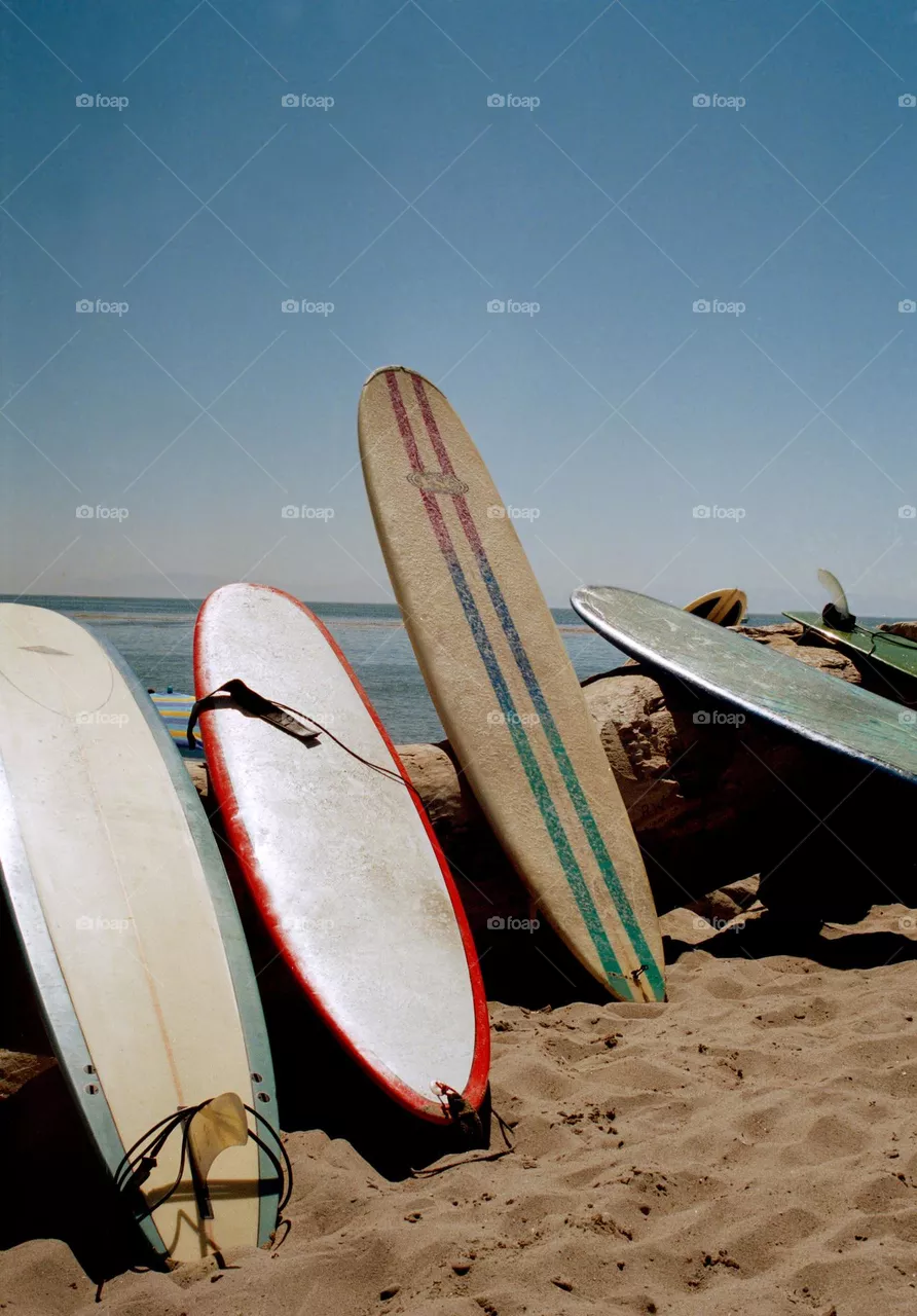 Vintage looking surfboards in color on the beach with a retro style almost like it’s the 60s on a beautiful day to go surfing, go ride the waves 