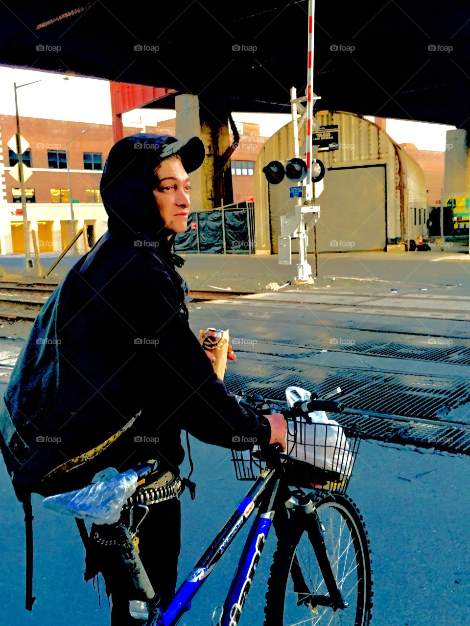 My friend wearing his hoodie closer up on his bicycle near the Pulaski Bridge and the train tracks in Long Island City, Queens, New York. This picture was taken in the Spring of 2019. Hypnotic Productions