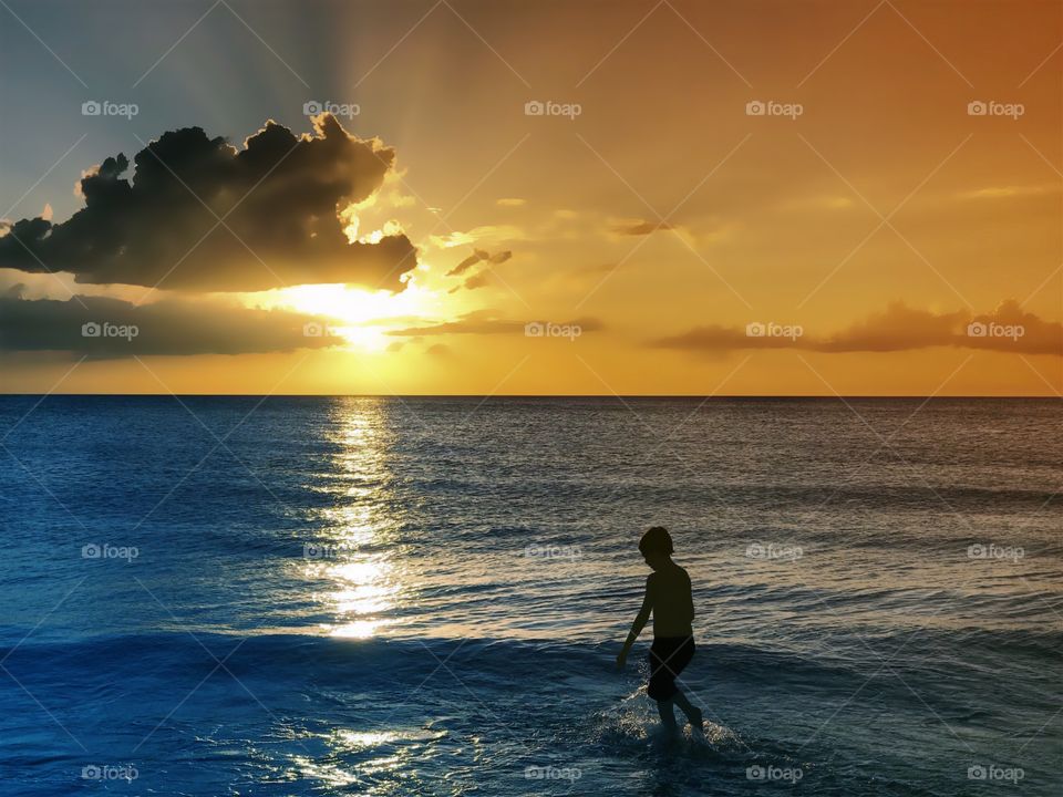 Small boy spending a joyous moment surrounded by a spectacular golden ocean sunset.