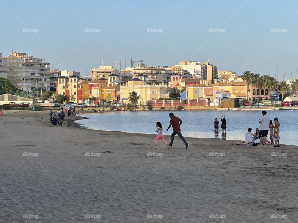 Not recognizable people doing different activities in the beach, father and daughter running at the beach, beach houses in the background 