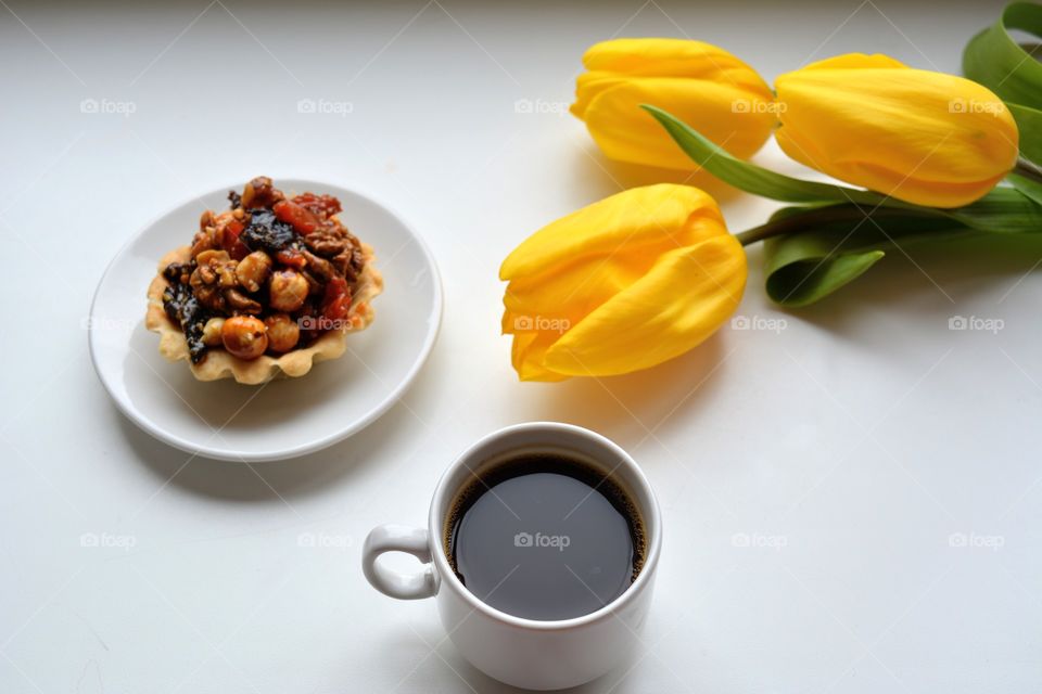 cup of coffee with cupcake on a plate and tulips flowers on a white background, morning routine