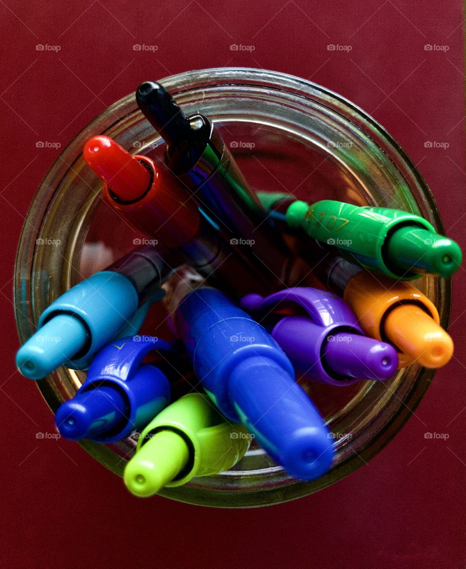 Colorful pens in glass mason jar on red desktop 