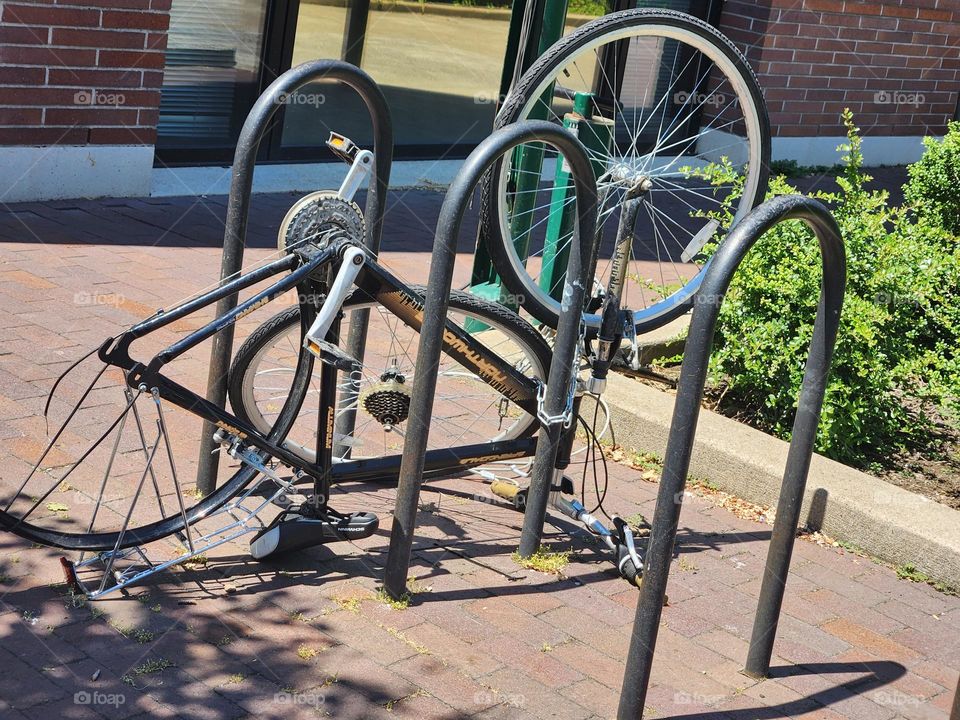 Northwoods bicycle missing a wheel chained to bike rack up-side down in front of Urban building