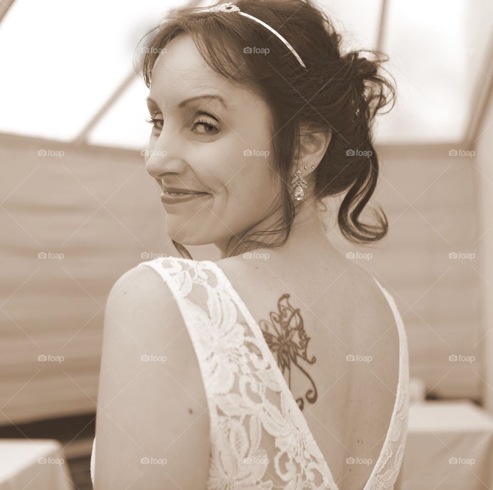 Cheeky tattooed bride. Over the shoulder glance. Butterfly tattoo and lace wedding dress. 