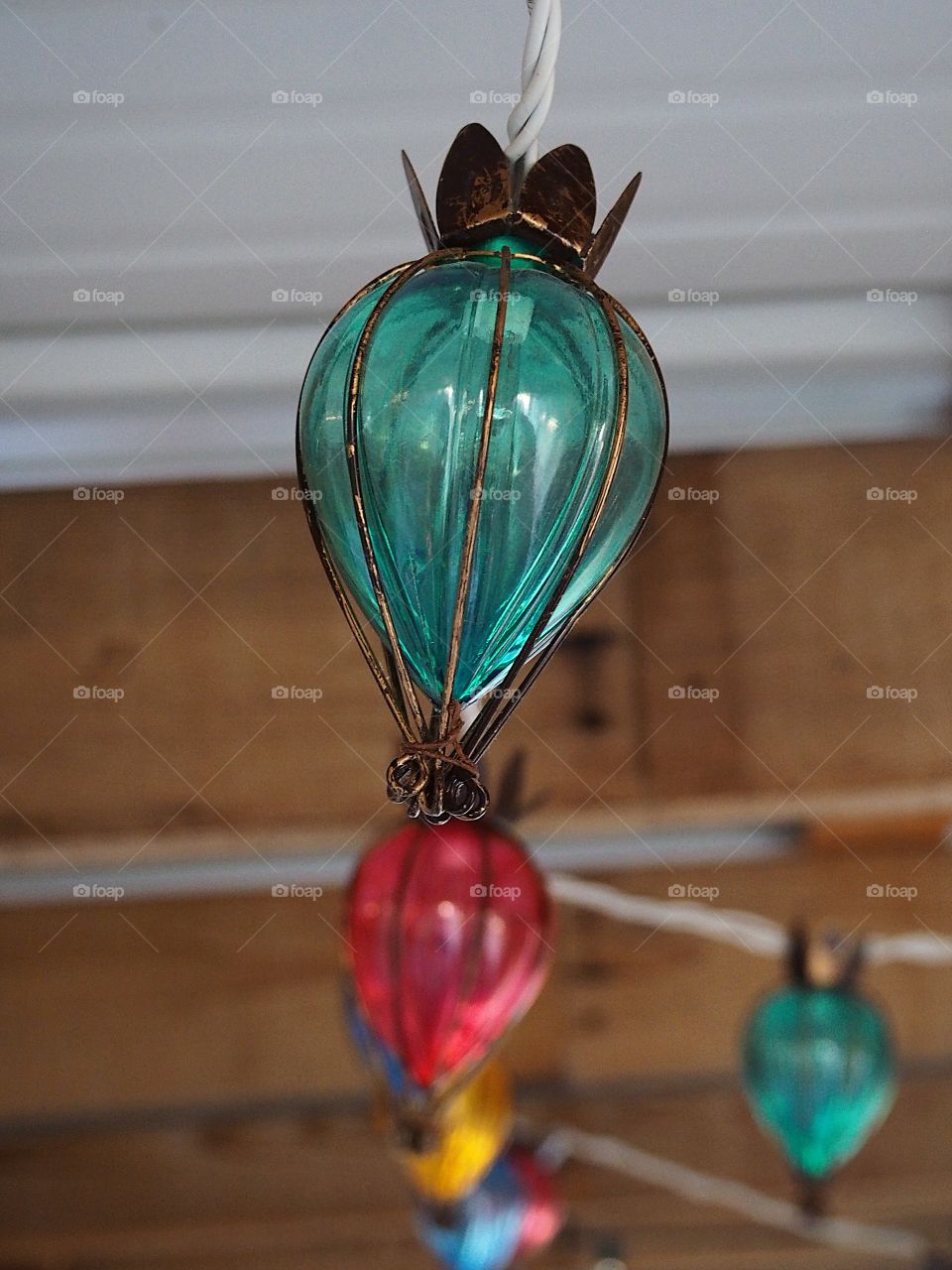 A turquoise outdoor decorative light with thick wire accents close up with a string of blurred lights of other colors in the background. 