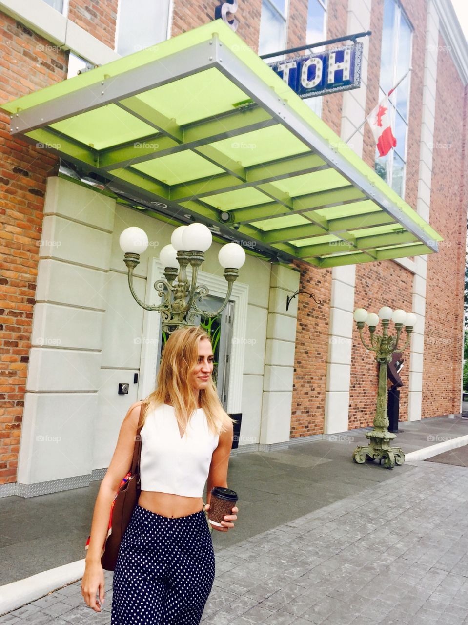 Blonde woman standing in front of hotel and holding coffee