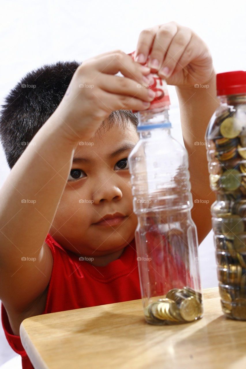 Little boy putting money in a bottle