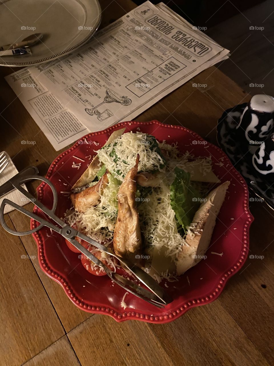 Chicken Caesar salad on a red plate with tongs