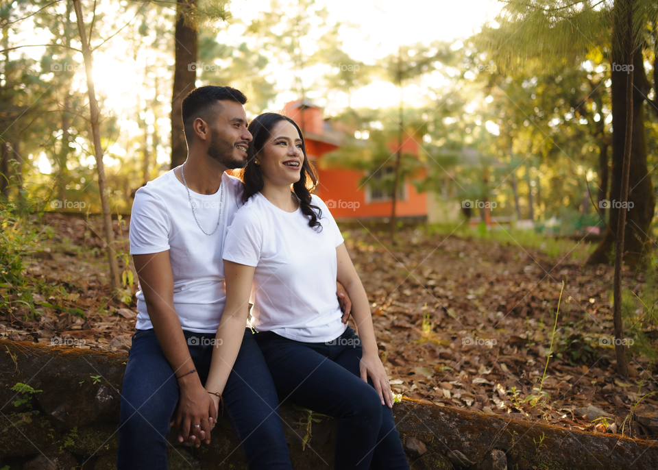 Couples of young people sitting in middle of the forest while looking smiling and happy, in a sunny day.