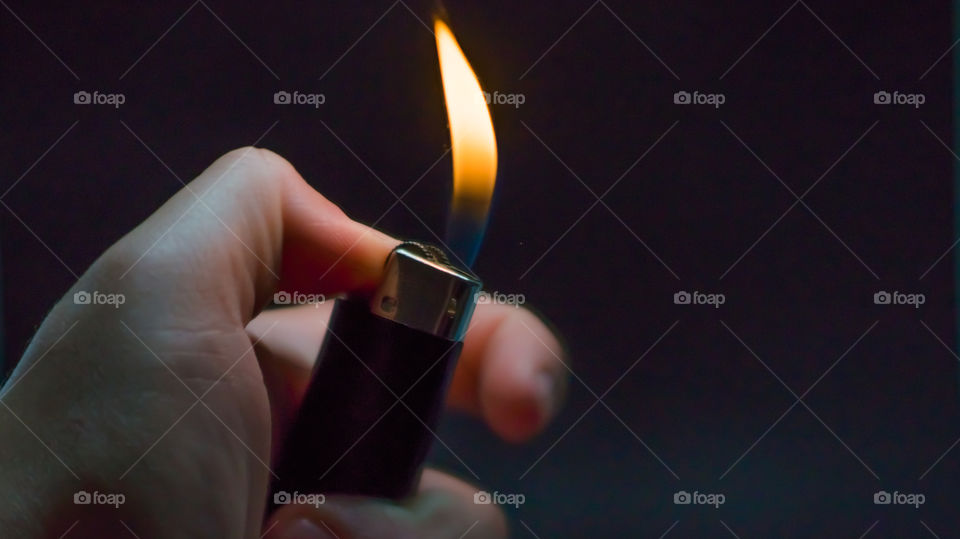 A person has lighters in his hands and he lights it through a flint wheel, the lighter ignites, sparks and fire appear, close-up on a black background.