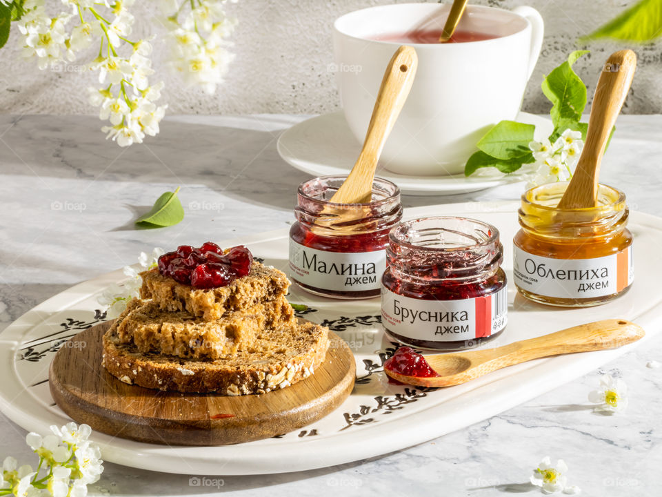 Bread and different sorts of marmalade on a white table decorated with white flowers 