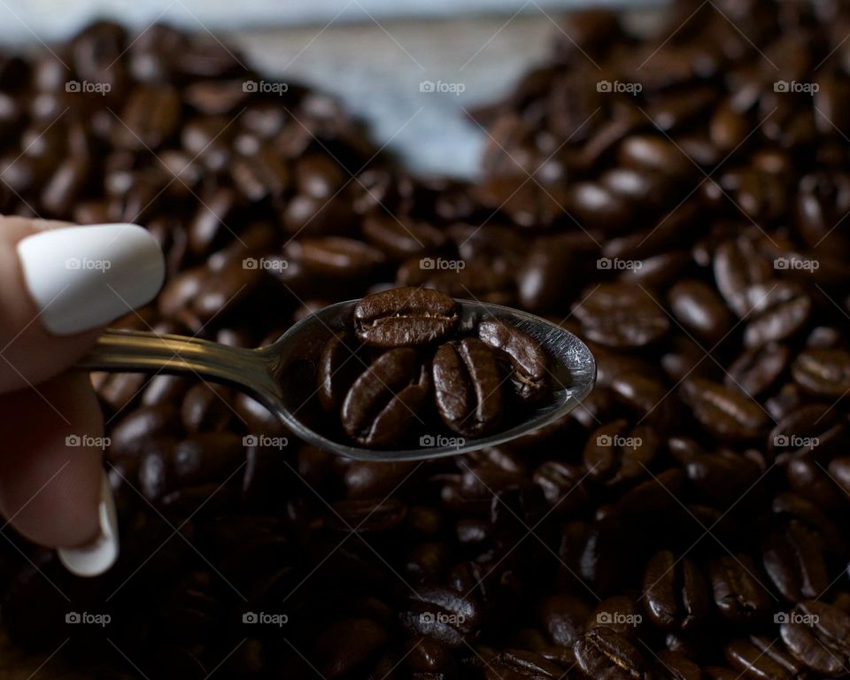 Woman holding a teaspoon of Coffee Beans