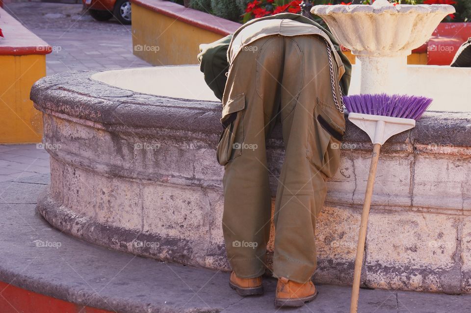 A back view of a man performing maintenance at old turned off water fountain.