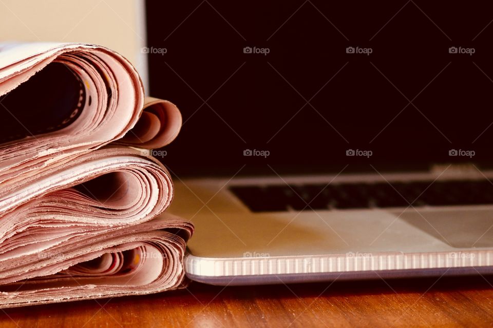 Stack of folded newspapers closeup on wood office desk beside laptop computer, concept business and finance, reading and education, learning and current events, IT and technology, closeup 