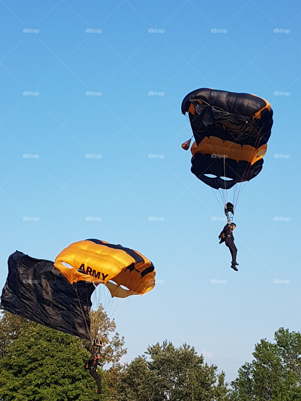 Two US Army Golden Knights parachuting onto the ground from bright blue skies