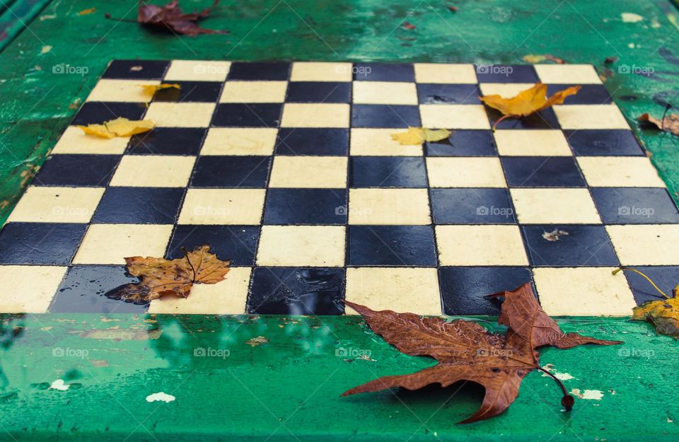 Abandoned wet chessboard with fallen autumn leaves.