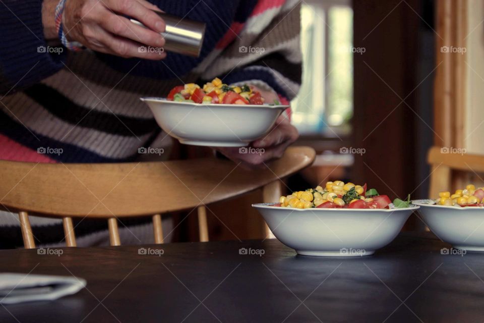 View of a table with salad bowl and woman holding a salt shaker
