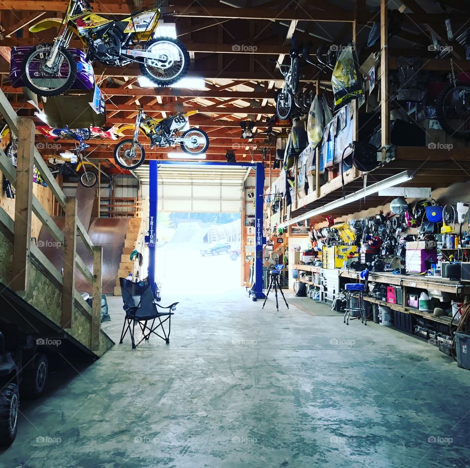 Motorcycles hanging from the rafters of a large workshop man cave with a garage door opened to let the gorgeous summer sunshine in. 