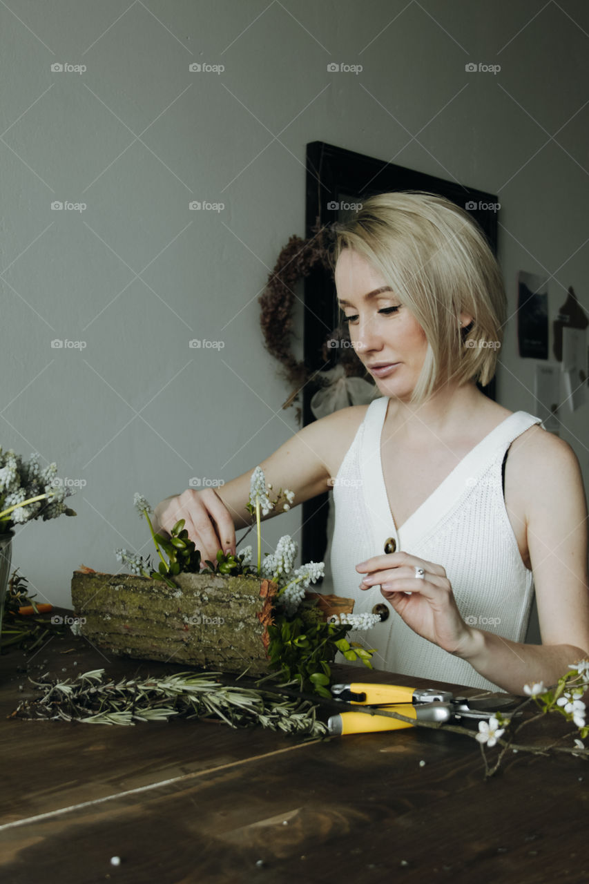 Beautiful blonde woman is making flower and wooden composition with muskari  on the table 