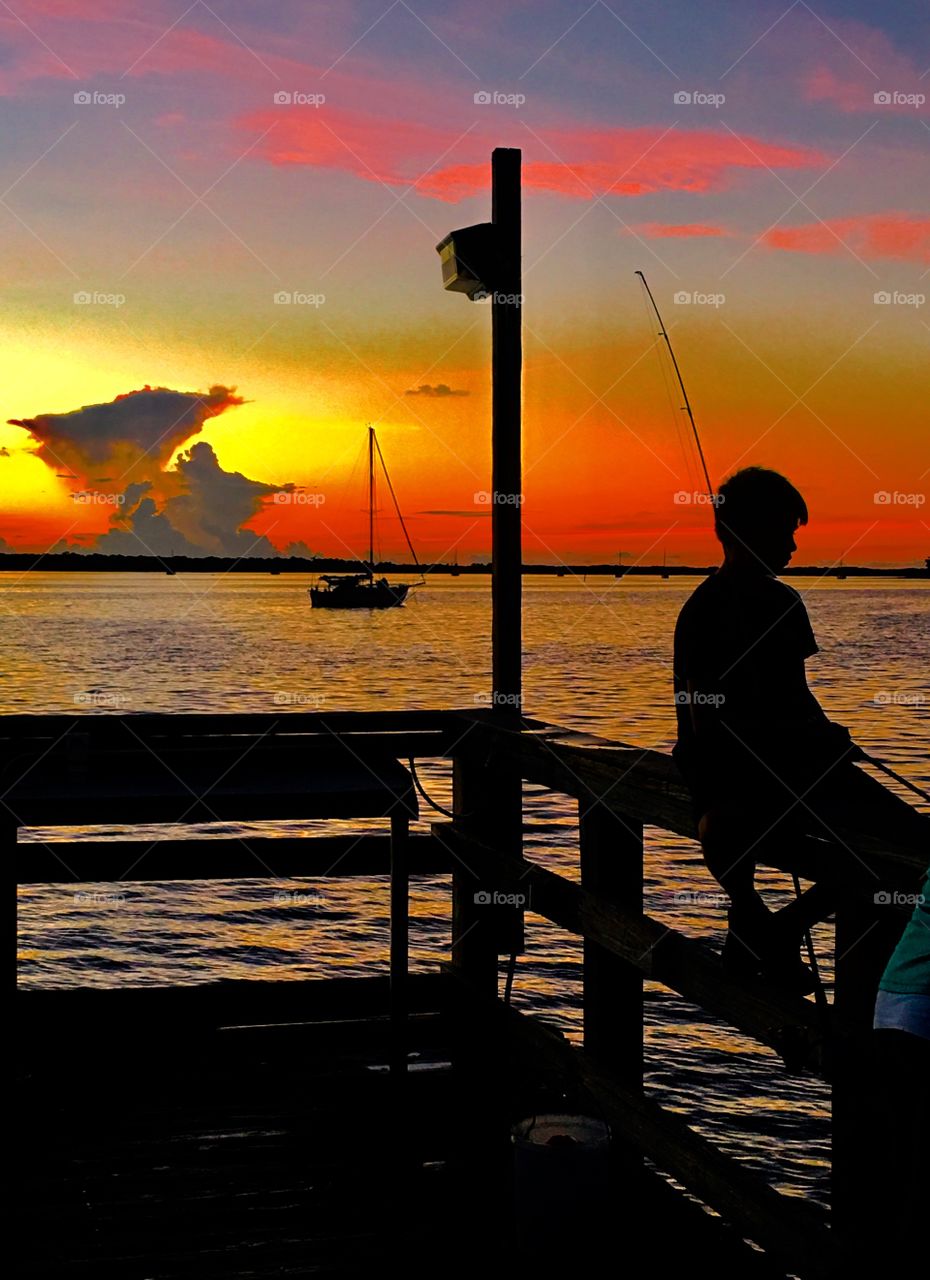 Boy fishing on pier at Sunset
