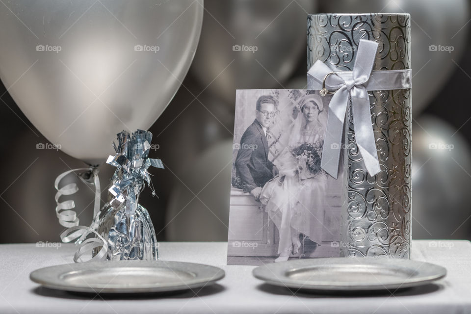 monochrome image of silver anniversary party using different shades of gray with pewter plates, black and white photo, silver gift box and party favors in front silver balloon background