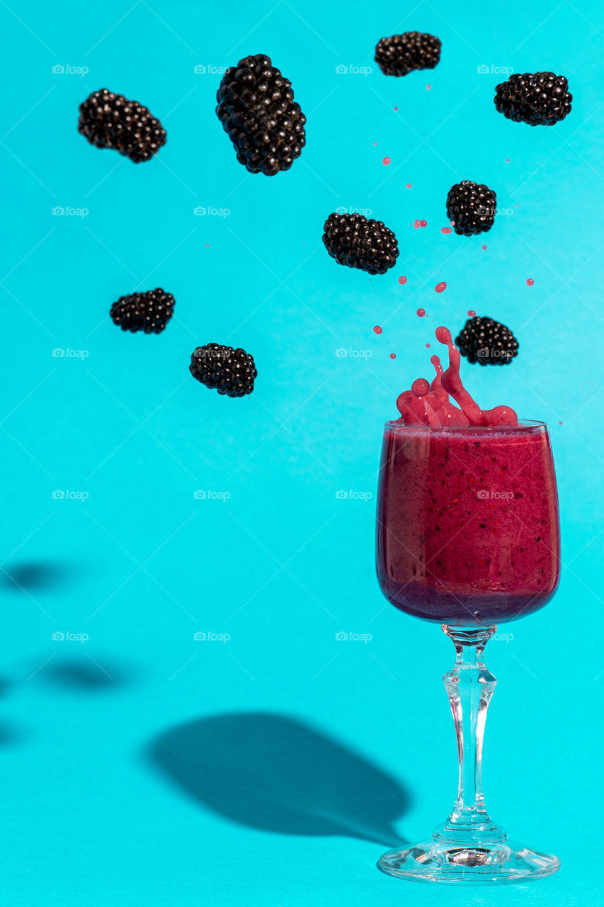 Blackberry smoothie with blackeries falling. Pastel blue background