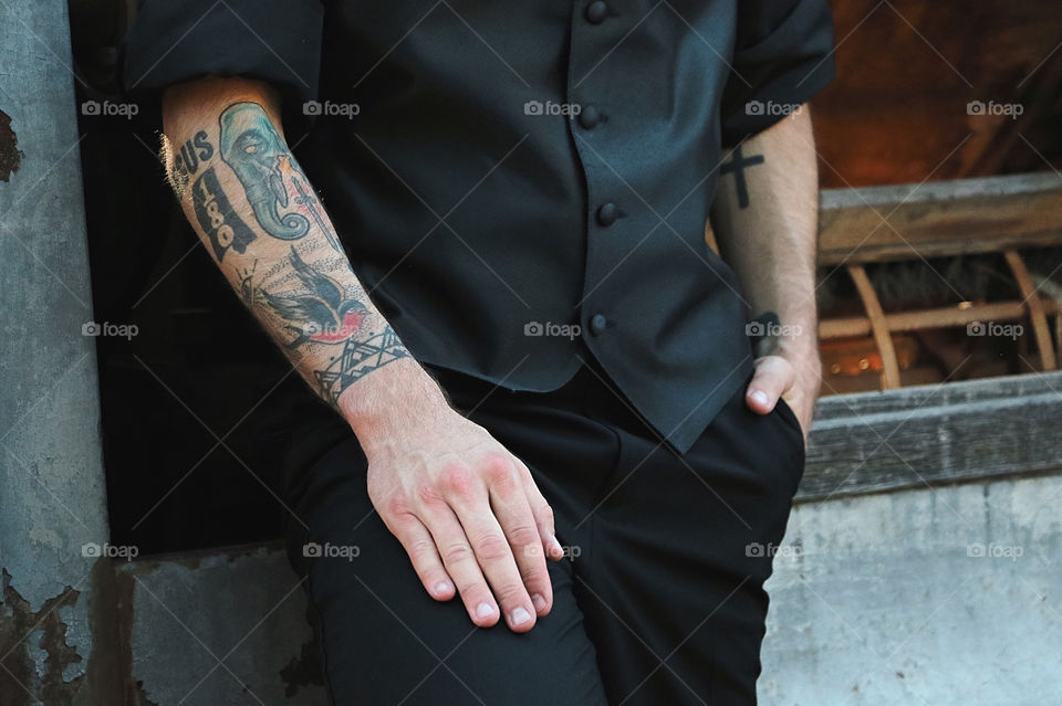 Young male with tattoos standing in a vest and dress pants