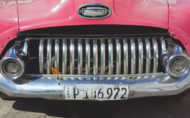 The front grille and headlights of a pink classic American car parked in Havana, Cuba.