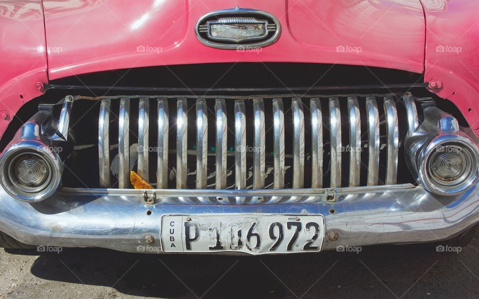 The front grille and headlights of a pink classic American car parked in Havana, Cuba.