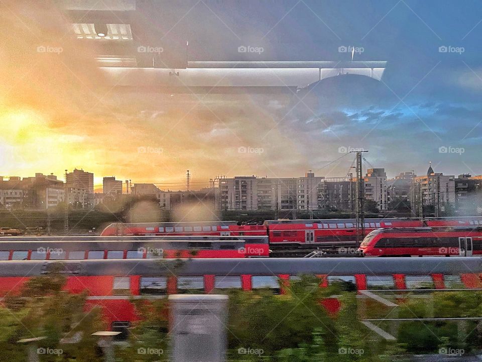 Looking through a train window at red moving passenger trains at sunset