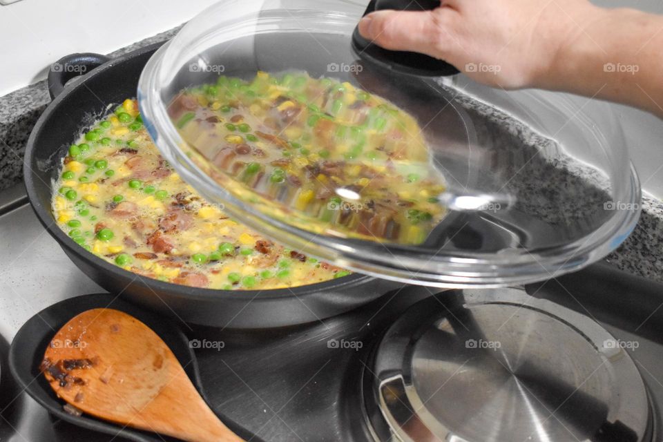 Homecooking cooking Frittata at home and adding and mixing ingredients and removing the Frittata from the pan for cutting and serving on a white plate with tomatoes. Healthy home cooking in kitchen. Breakfast and lunch food preparation.