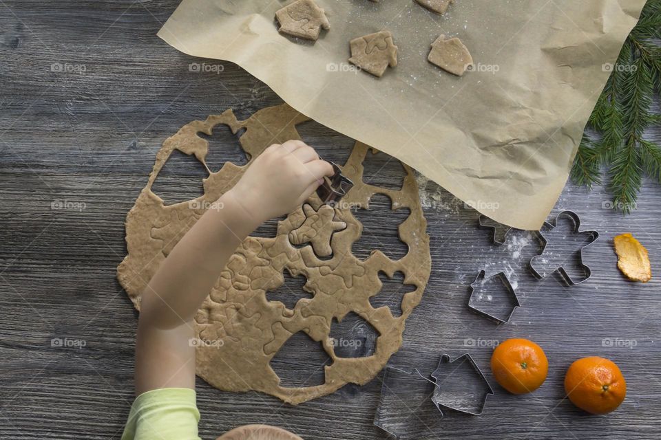 A small child helps to prepare festive, gingerbread cookies on a wooden table on Christmas Eve.