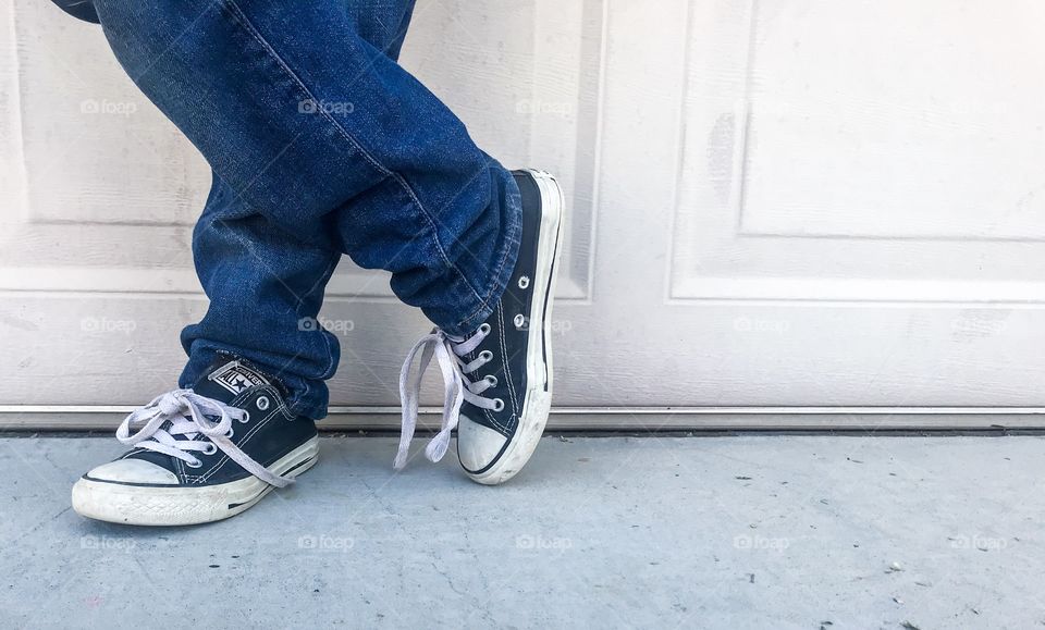Boy with legs crossed wearing blue jeans and converse style shoes 