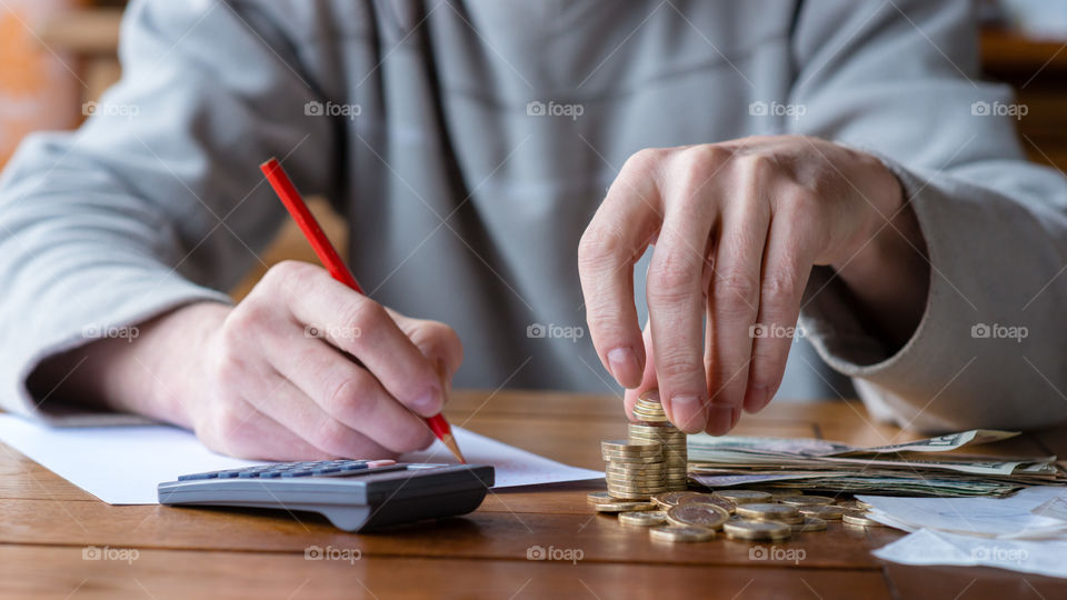 clouse-up man with calculator counting, making notes at home, hand is writes in a notebook, stacked coins arranged at desk. Savings, finance concept.