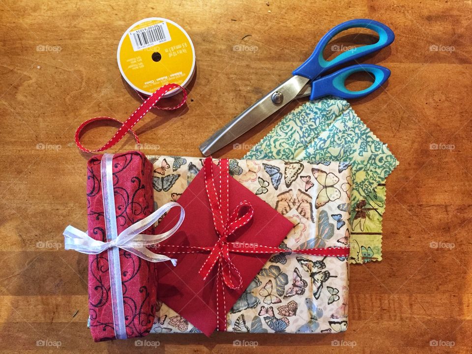 And assortment of Christmas gifts wrapped in patterned cloth and fabric bows. A pair of pinking shears and a spool of ribbon sit nearby