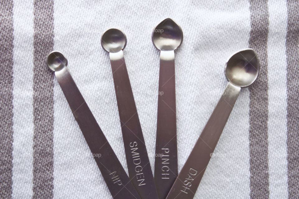Overhead view of miniature stainless steel measuring spoons on a white-and-grey-striped dish towel