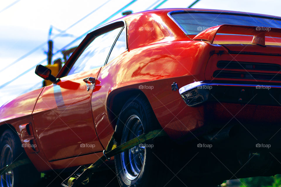 A blazing red Pontiac Firebird rides atop a flat bed tow truck.