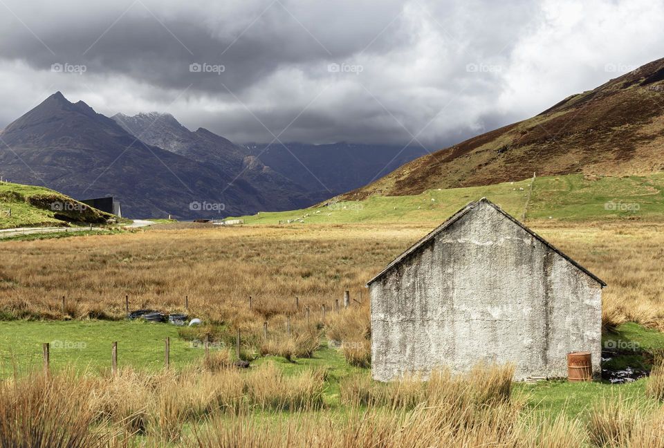 The Cuillin Mountains overlooking sheep grazing in fields with an old barn in the foreground 